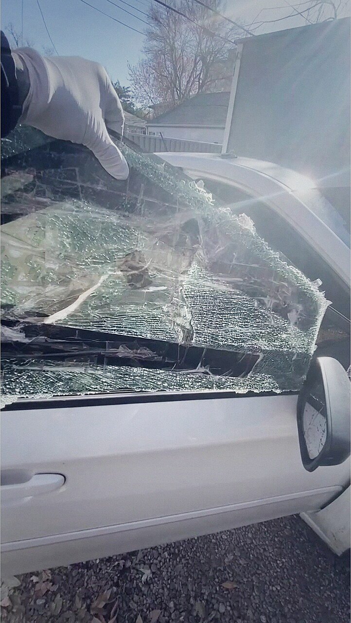 Technician lifting shattered door glass from a sedan during cleanup